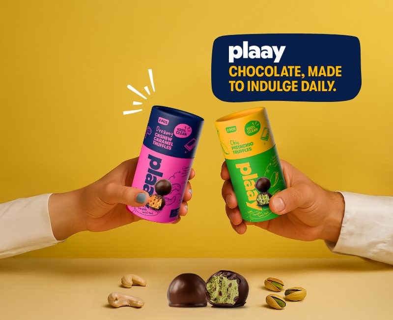 Two hands holding Plaay chocolate tubes on a yellow background